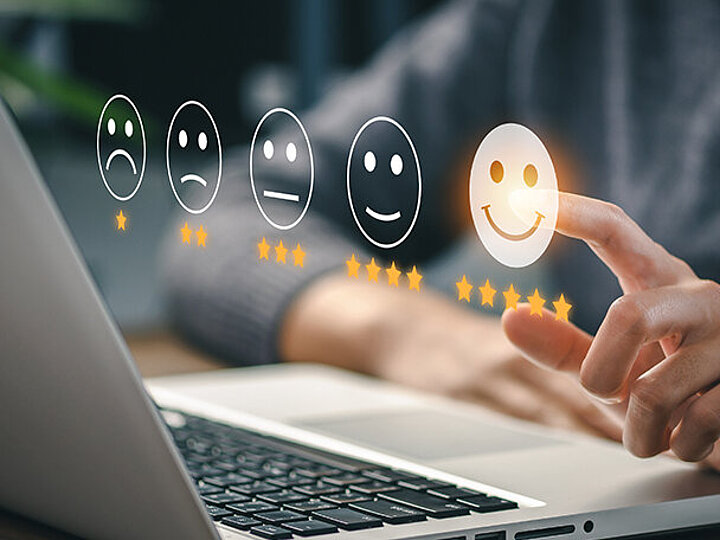 Über einem Laptop schweben vier Smilies, ein Mann zeigt auf den Lächelnden